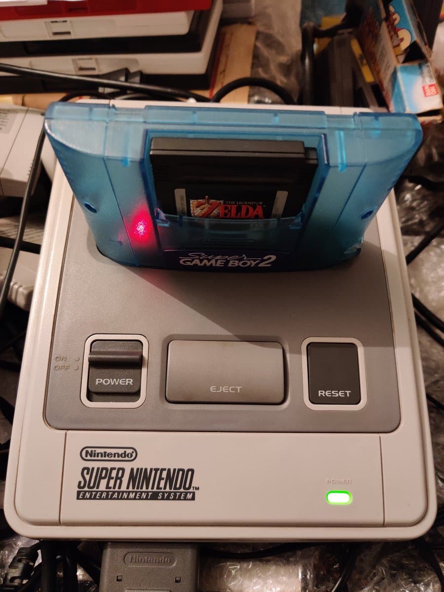 Super Nintendo with Super Game Boy 2 cartridge inserted; red power LED illuminated, green power indicator visible on console.