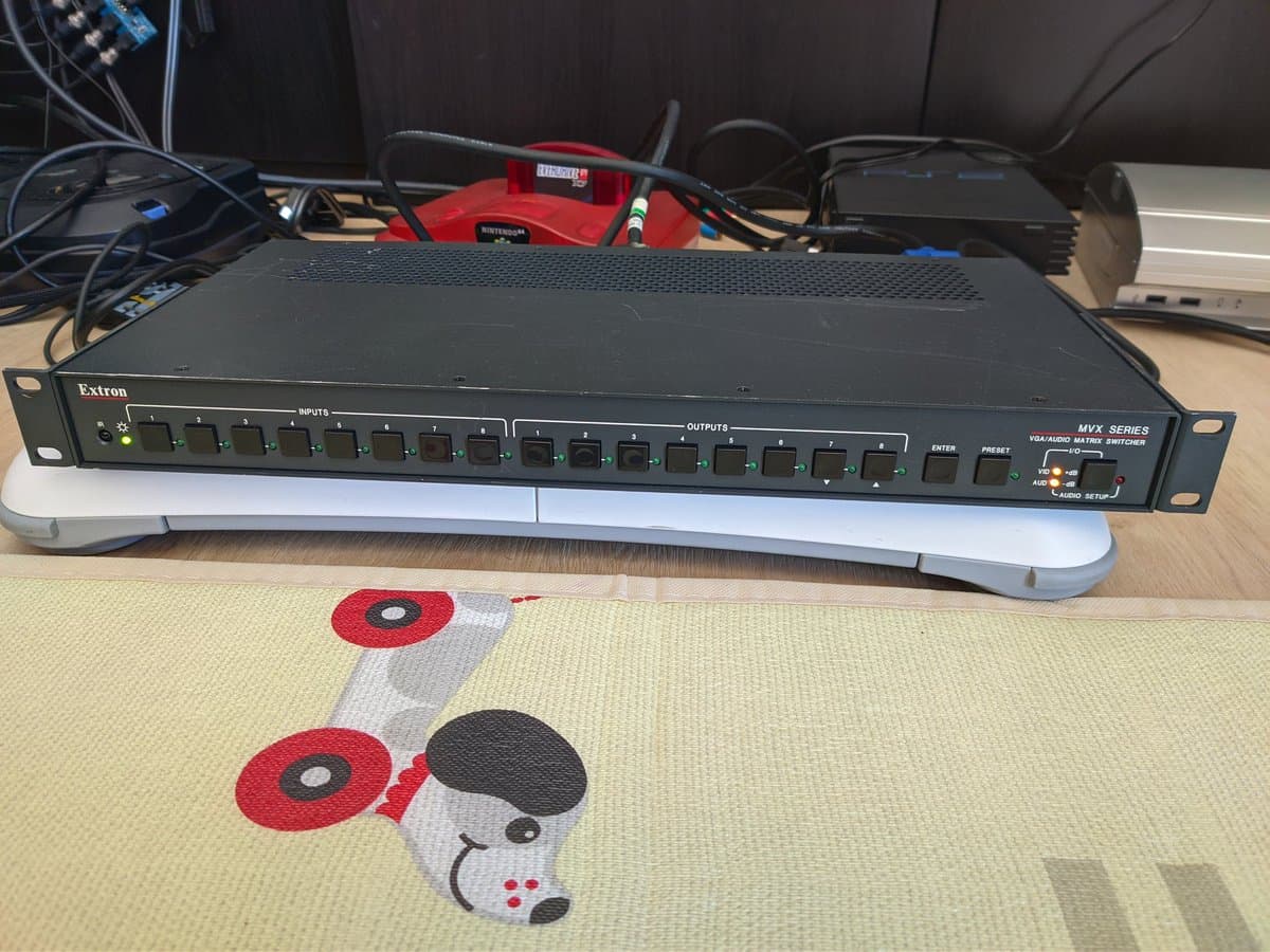 Extron MVX Series video switcher on desk with Nintendo 64 controller and red/black gaming peripherals visible in background setup.