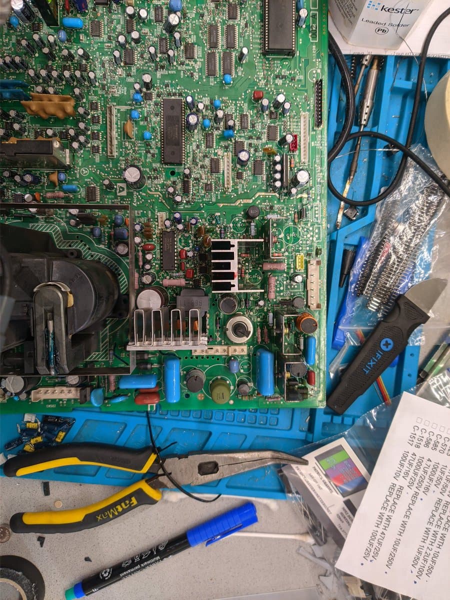 Sony PVM-14M4J C board during retrace line repair; capacitor kit, soldering iron, multimeter, and desoldering tools visible on work surface.