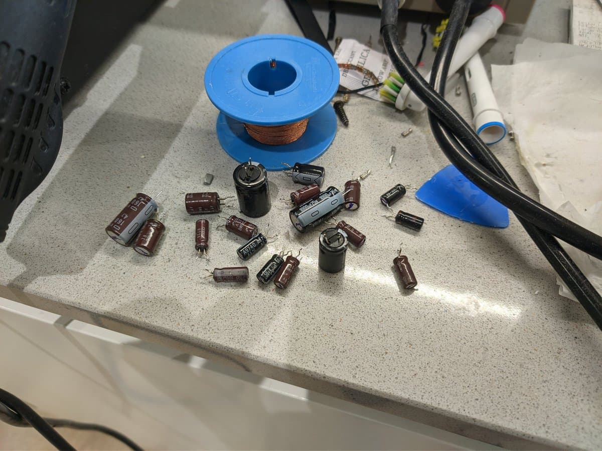Disassembled electrolytic capacitors and components from Sony PVM-14M4J, including cylindrical caps, resistors, and a spool of copper wire on workbench.