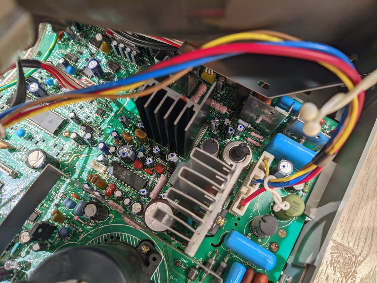 Close-up of Sony PVM-14M4J A board showing reflowed solder joints, replaced capacitors marked with dots, heat sinks, and multicolored power cables during retrace line repair.