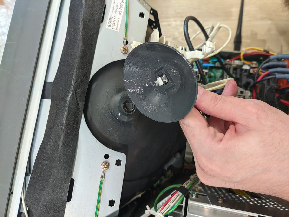 Hand holding Sony PVM-14M4J anode cap with dielectric grease applied, workbench with circuit boards and wiring visible behind.