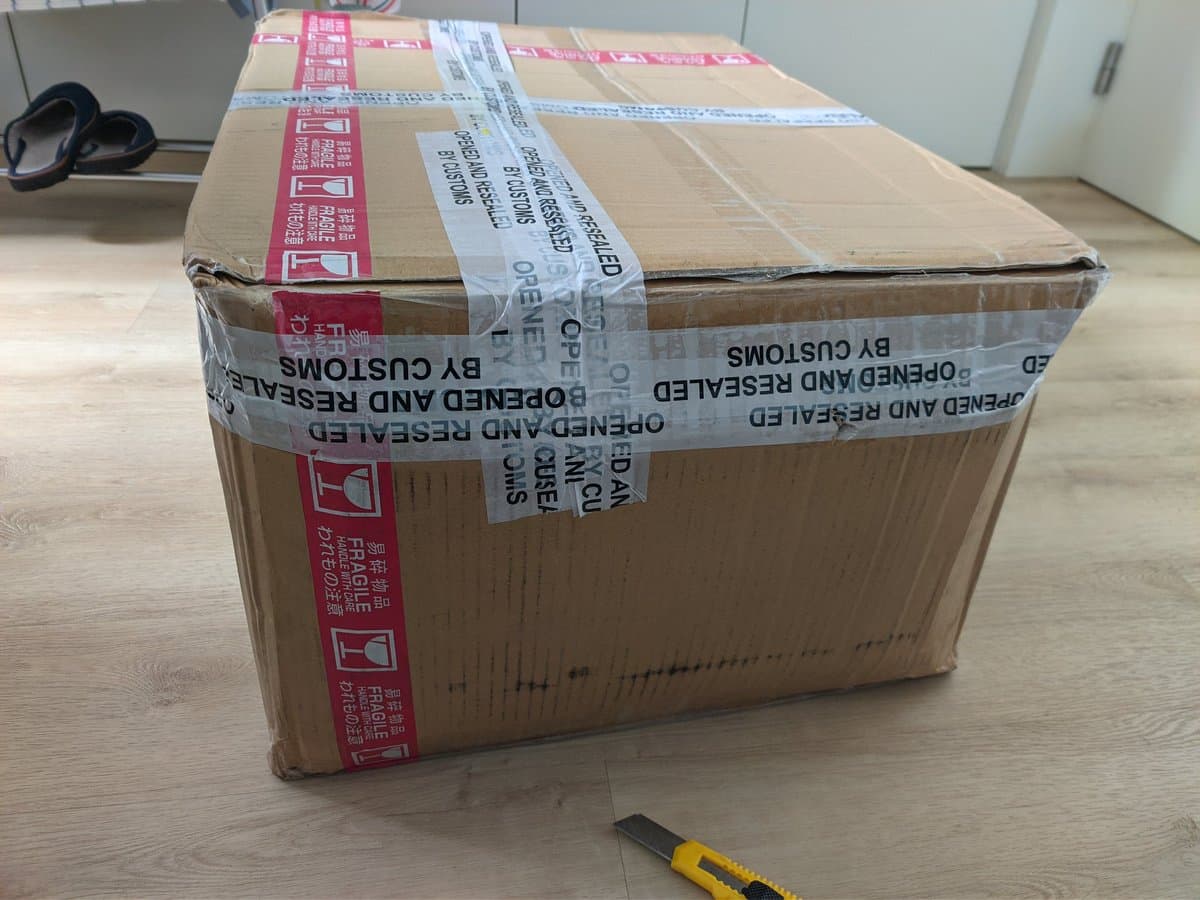 Cardboard shipping box for three Sony PVM-9040 CRT monitors with red and blue customs tape, showing external damage from rough handling during international transit from Japan.