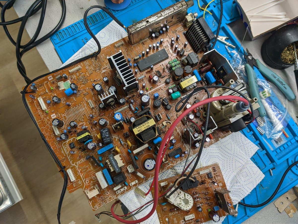 Sony KV-29FX30E main PCB undergoing recap, showing replaced capacitors, heatsinks, and transformer with soldering work in progress on blue service board.