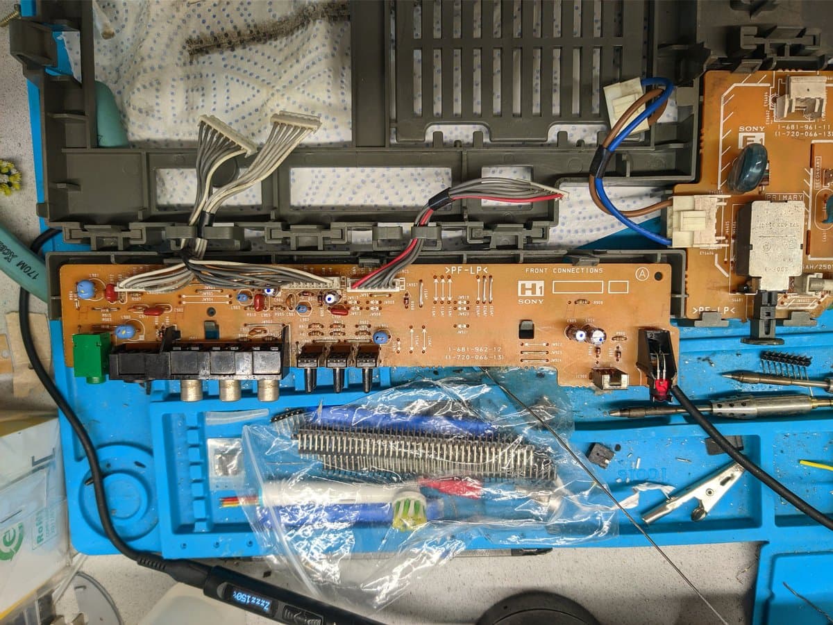 Sony KV-29FX30E power supply board mid-recap: orange PCB with new capacitors in plastic bag, desoldering tools, and rewired front connections visible.