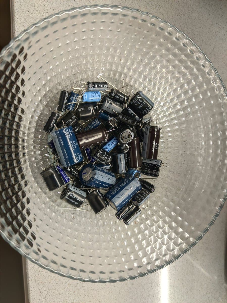 Basket of 51 failed electrolytic capacitors removed from three Sony PVM-9040 monitors during restoration, blue and black cylindrical components.