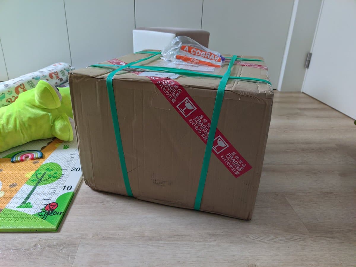 Cardboard shipping box secured with green straps and red fragile label, containing Sony BVM-D9H5J CRT monitor arrival from Japan.