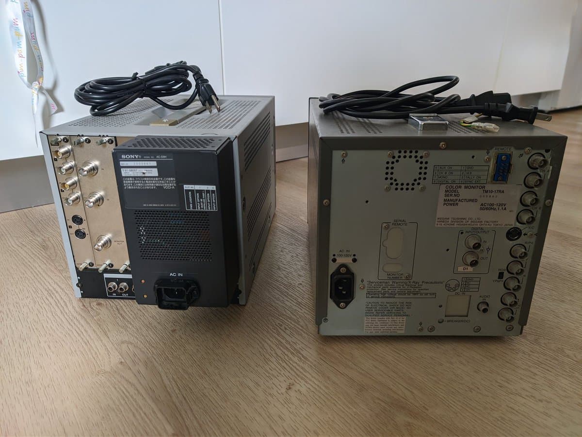 Two CRT monitors on wooden surface: Sony BVM-D9H5J (left, black, with coiled power cable) and Ikegami TM10-17RA (right, beige, with BKM-127W card visible).