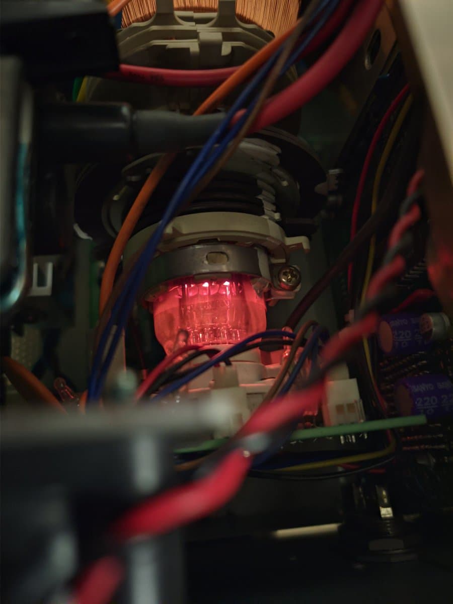Red illuminated component surrounded by multicolored wires inside Ikegami monitor chassis during voltage reconfiguration work.
