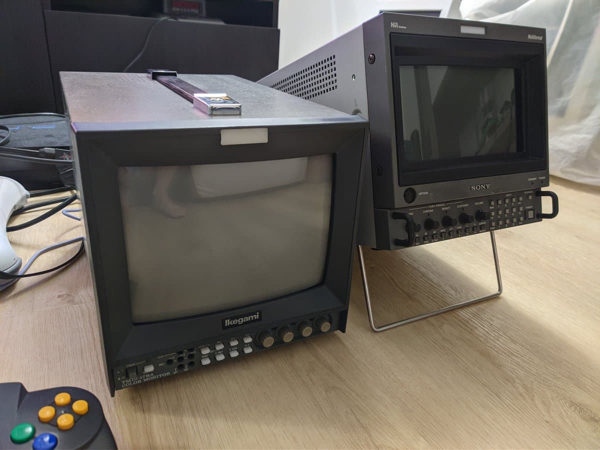 Ikegami and Sony professional CRT monitors on workbench with game controller, showing retro gaming setup during restoration work.
