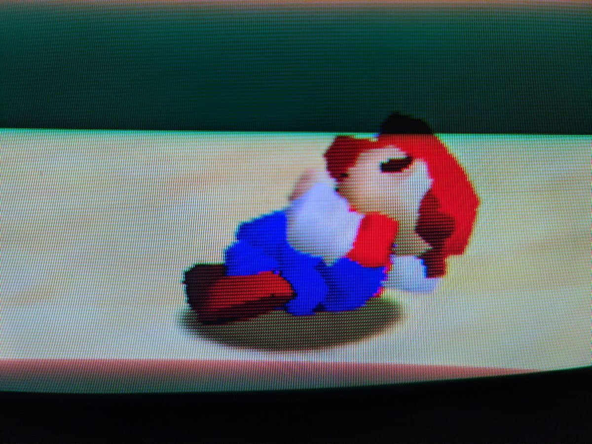 Pixelated Mario character with red hair and blue outfit lying on brown ground, displayed on restored Sony BVM-D9H5J CRT monitor.