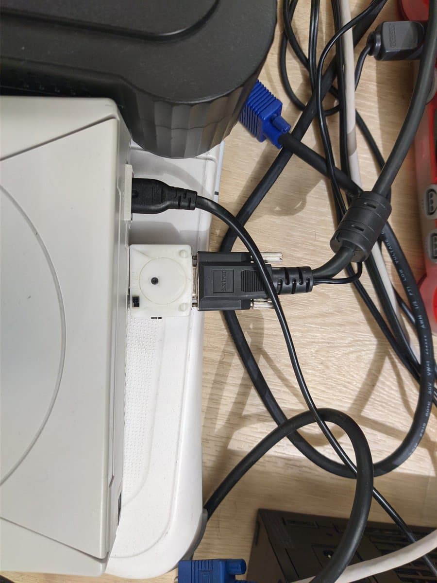 White power strip with black cables and blue VGA connector plugged in, wooden desk surface, CRT monitor visible above.