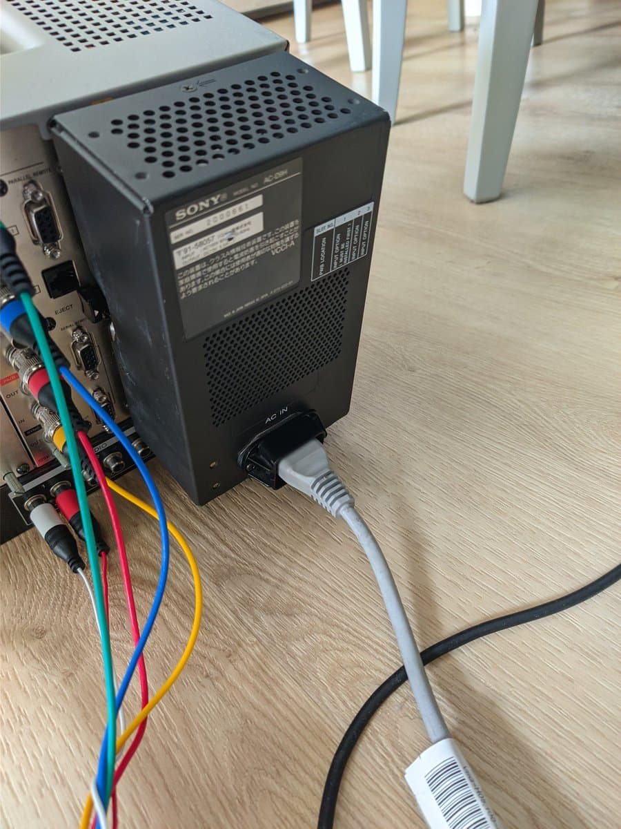Sony BVM-D9H5J power supply undergoing recapping work, partially disassembled with colorful internal wiring visible and AC power cable connected for testing.