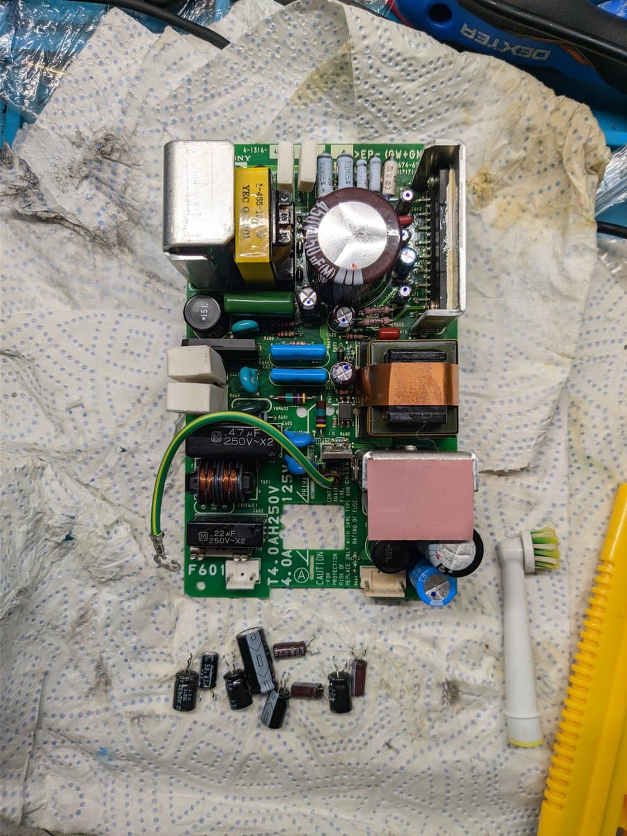 BVM-D9H5J PSU board with partially recapped capacitors, large filtering cap, transformer, and removed electrolytic capacitors laid out below during maintenance work.