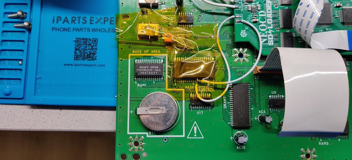 Neo Geo CD circuit board showing F-RAM upgrade with coin battery, IC chips labeled SONY JAPAN, and heat-sinked components on green PCB.