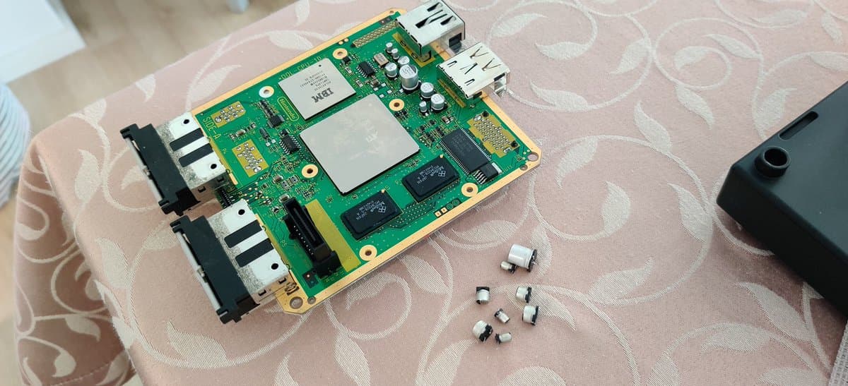 GameCube motherboard with Xeno modchip installed, showing CPU, RAM, and associated circuitry with several desoldered components nearby.