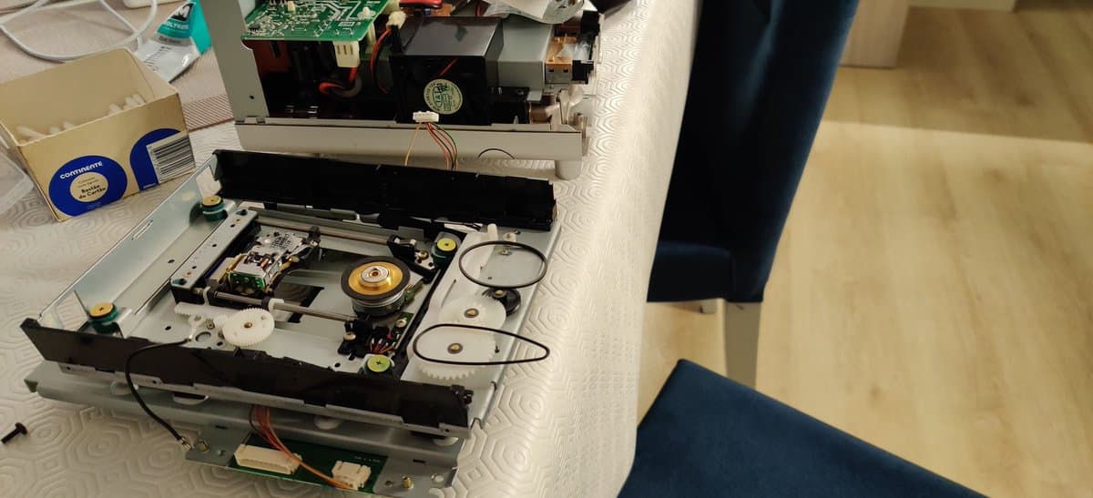 Panasonic Q optical drive disassembled showing internal mechanism with shattered left rail, deformed drive belt, and yellow spindle motor visible during restoration work.