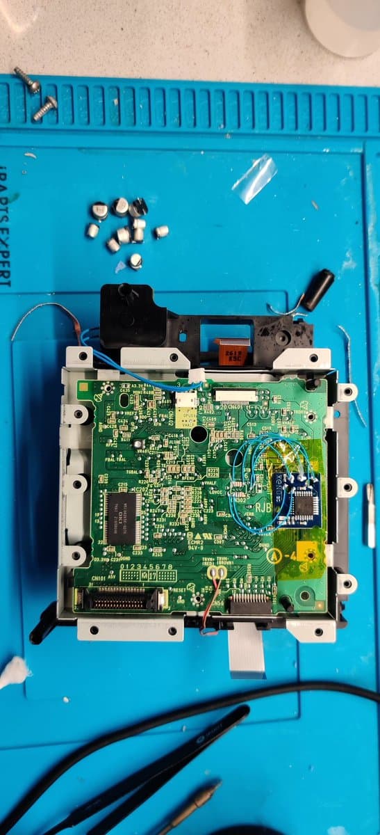 GameCube motherboard during Xeno chip installation, with recapped capacitors visible at top and modchip wiring in progress on blue work mat.