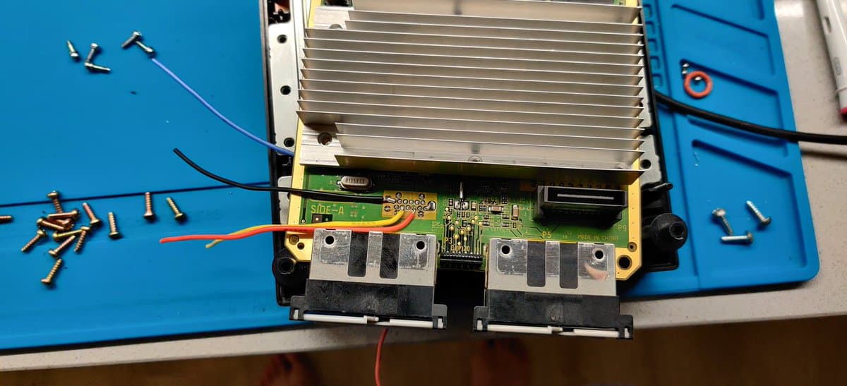 GameCube mainboard undergoing PicoBoot mod, showing green PCB with WiiKey interface, aluminum heatsink, capacitors, and scattered screws on blue workmat.