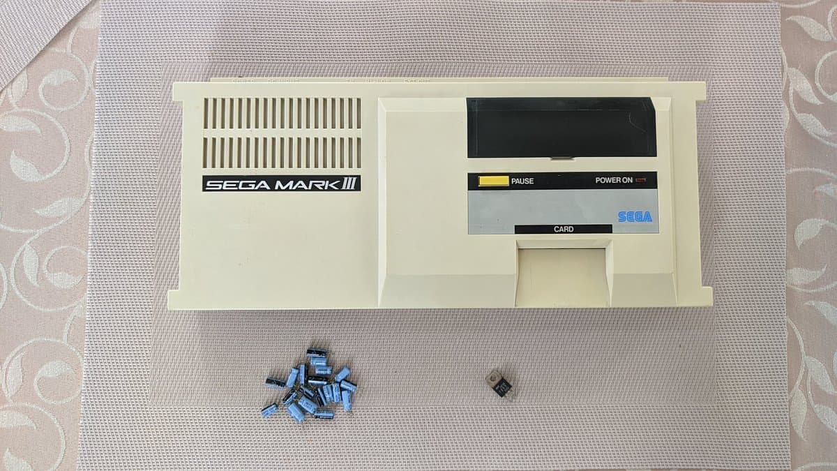 Sega Mark III console with open case showing card slot, pause and power buttons, blue capacitors and small component removed during retrobrighting restoration.