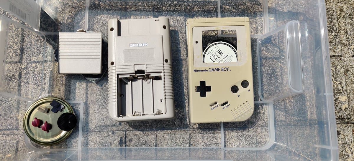 Original Game Boy DMG disassembled showing retrobrighted shell, battery cover, circuit board, and tools in storage container.