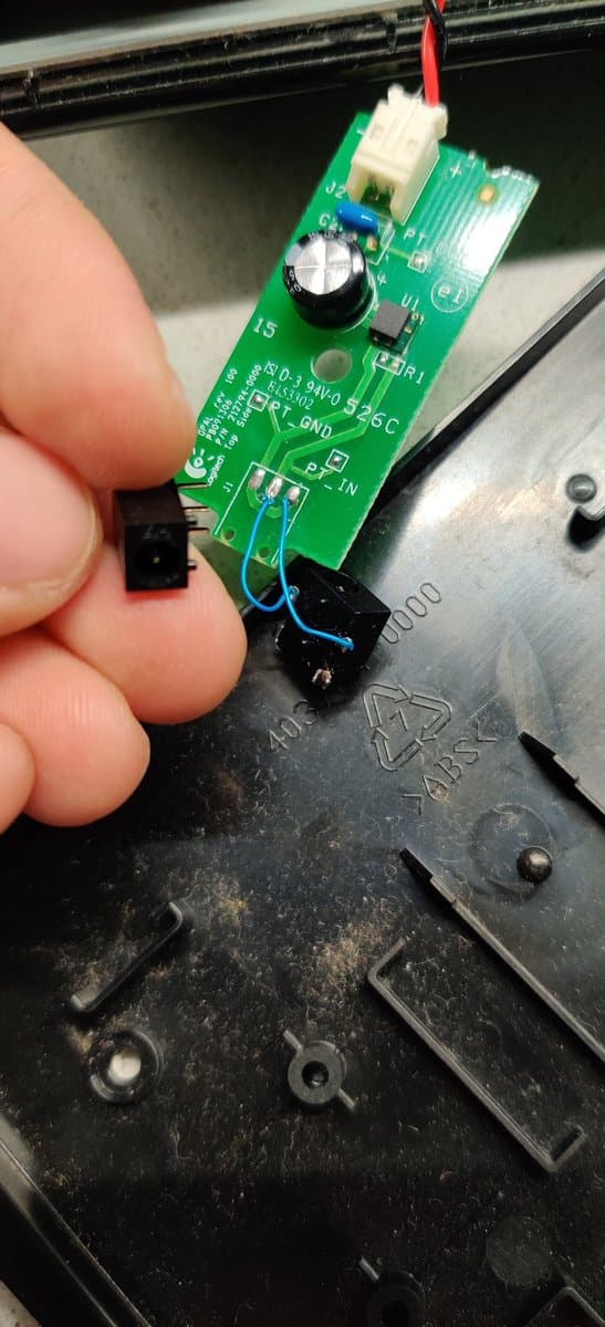 Close-up of repaired Logitech DiNovo Edge charging dock PCB with new barrel jack connector soldered in place, mounted on black plastic housing.