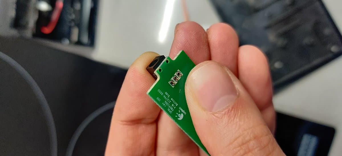 Green PCB with barrel jack connector held in hand, showing repaired charging dock for Logitech DiNovo Edge keyboard.