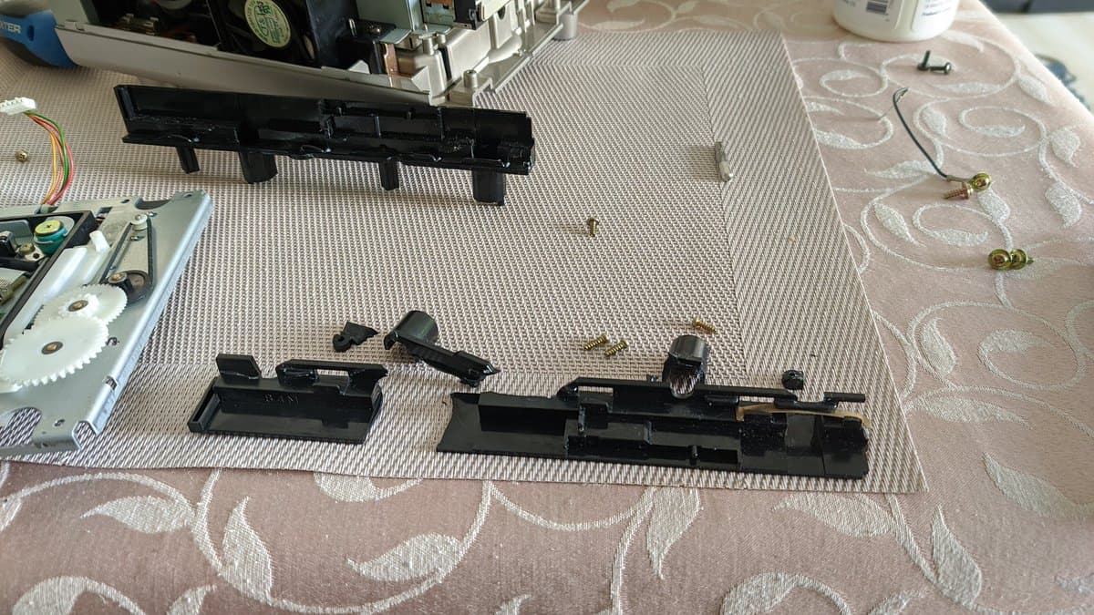 Disassembled Panasonic Q optical drive rails laid out for comparison; one 3D printed replacement rail next to original shattered rail pieces.