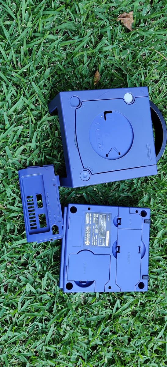 Disassembled Sega Saturn Model 2 plastic casing parts laid on grass showing retrobrite treatment progress, blue plastic shell components.