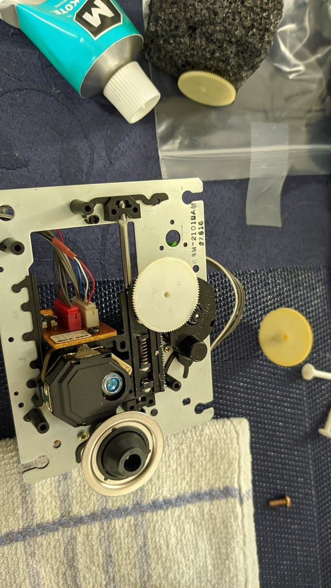 NEC PC Engine Super CD-ROM2 circuit board mid-recap with desoldering tool, replaced gears, and resistor component on paper towel nearby.