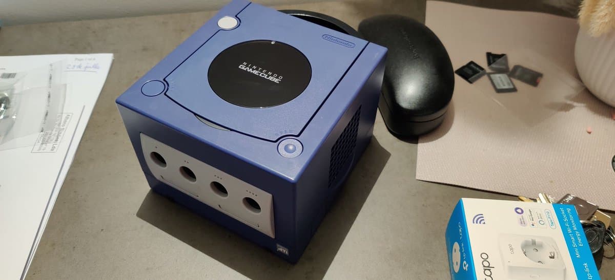 Indigo GameCube and retrobrighted Sega Saturn model 2 on work surface with documentation and wireless controller nearby.