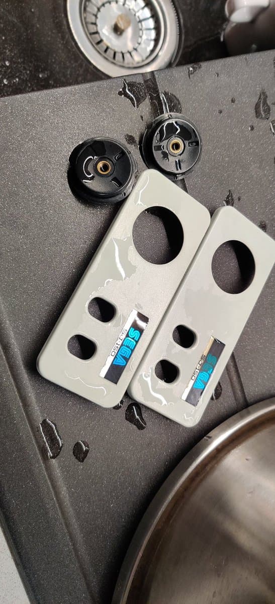 Disassembled Sega SG-1000 II controller parts showing retrobrighted white plastic shells with brass inserts and black internal components during restoration process.