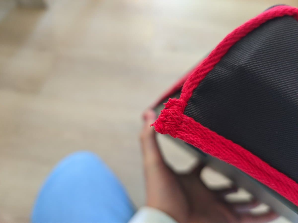 Close-up of frayed red fabric trim on black ZX Spectrum +2 dust cover, showing poor finishing quality.