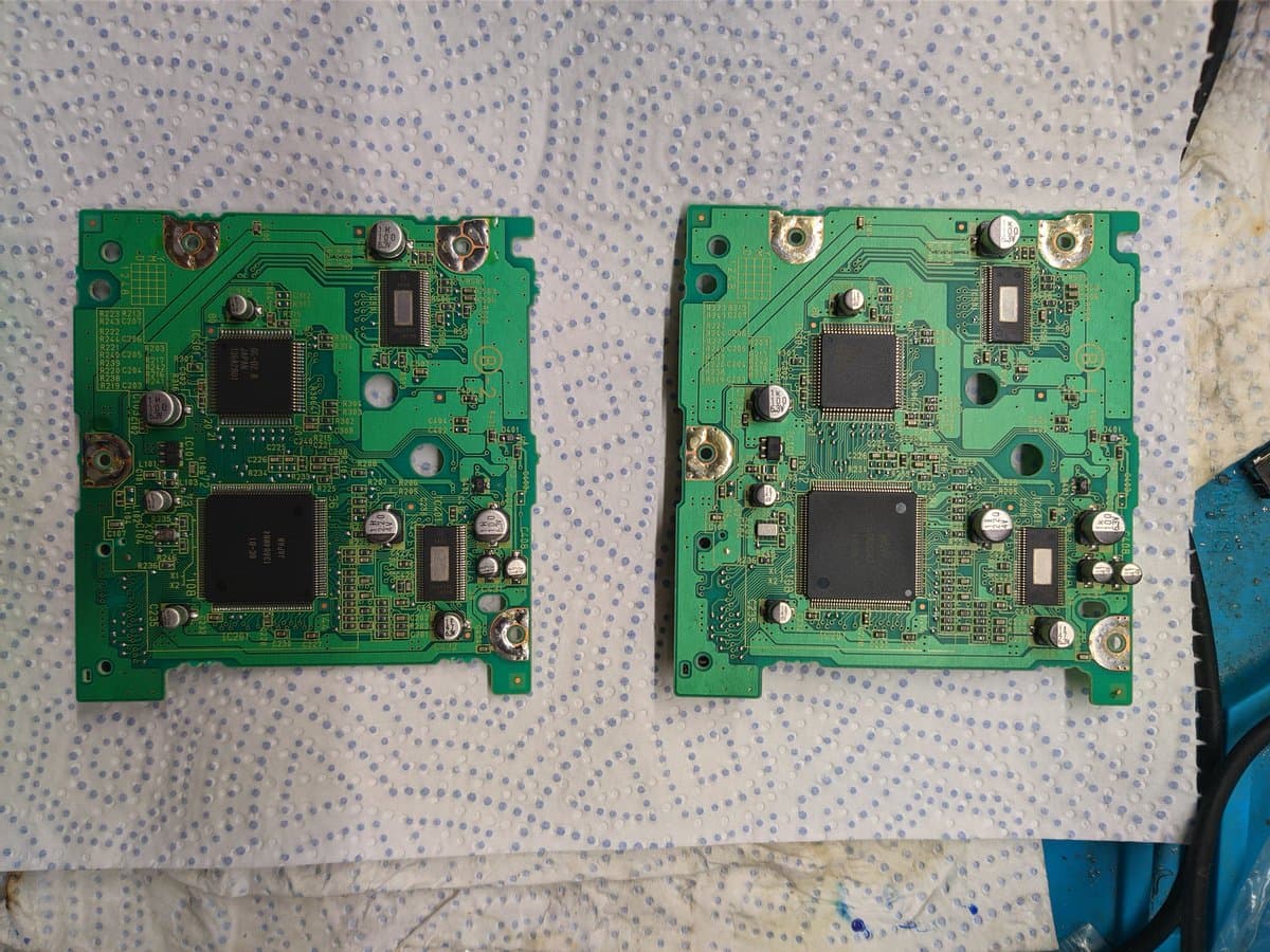 Two GameCube optical drive PCBs side-by-side after recapping. Left board revived, right board still dead with failed motor reading 30 ohms.