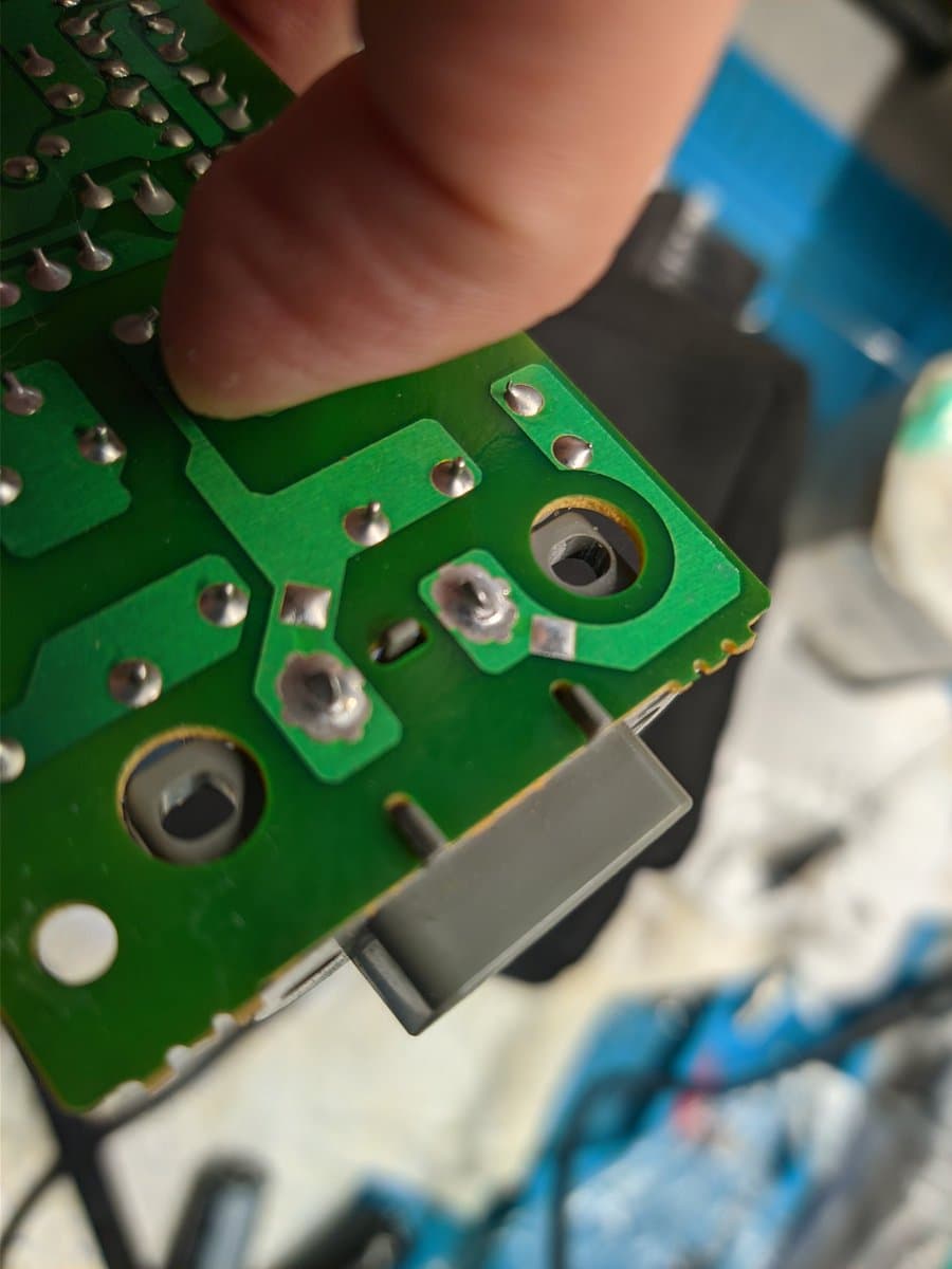 Close-up of PS1 power supply board showing cracked solder joints on power jack connector during preemptive recap repair.