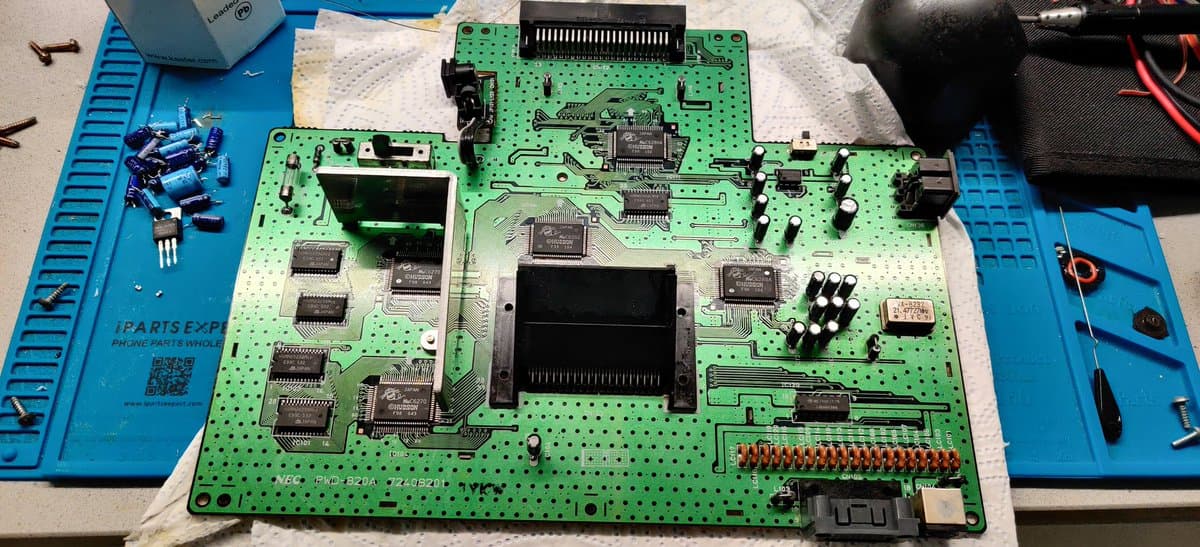 SuperGrafx main board during refurbishment: green PCB with new capacitors, voltage regulator, and visible chip components on blue work mat.