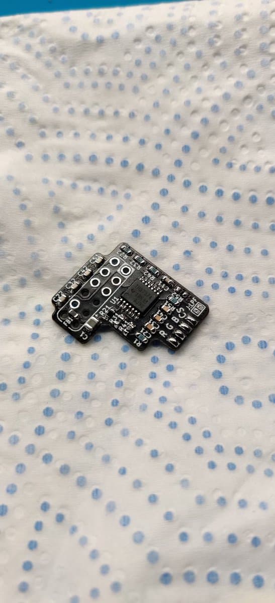 Small black PCB with multiple ICs and resistor arrays on dotted fabric surface during N64 RGB amp assembly.