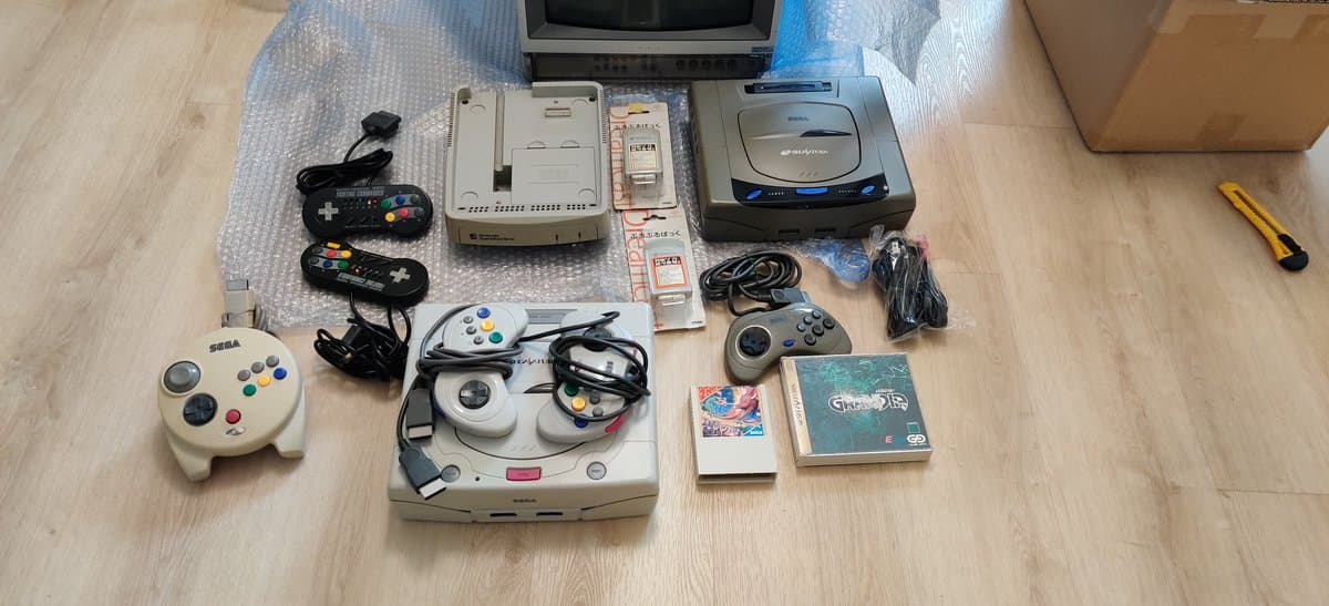 Sega Saturn consoles, controllers, games, Satellaview unit, and Sony PVM-14L2MD monitor displayed on wooden floor with accessories and cables.
