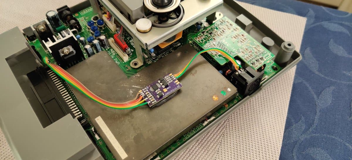 Interior of NEC PC Engine Super CD-ROM2 showing recapped power supply board, RGB amplifier module with rainbow ribbon cable, and 8-pin DIN connector installation during refurbishment.