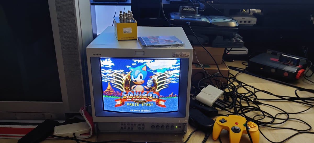 Sega Mega-CD 2 displaying Sonic the Hedgehog title screen on CRT monitor after fuse replacement repair, with yellow GameCube controller nearby.