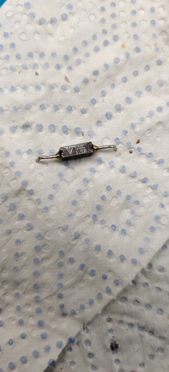 Axial fuse with wire leads on dotted fabric surface, component from Famicom repair with intermittent continuity issue.