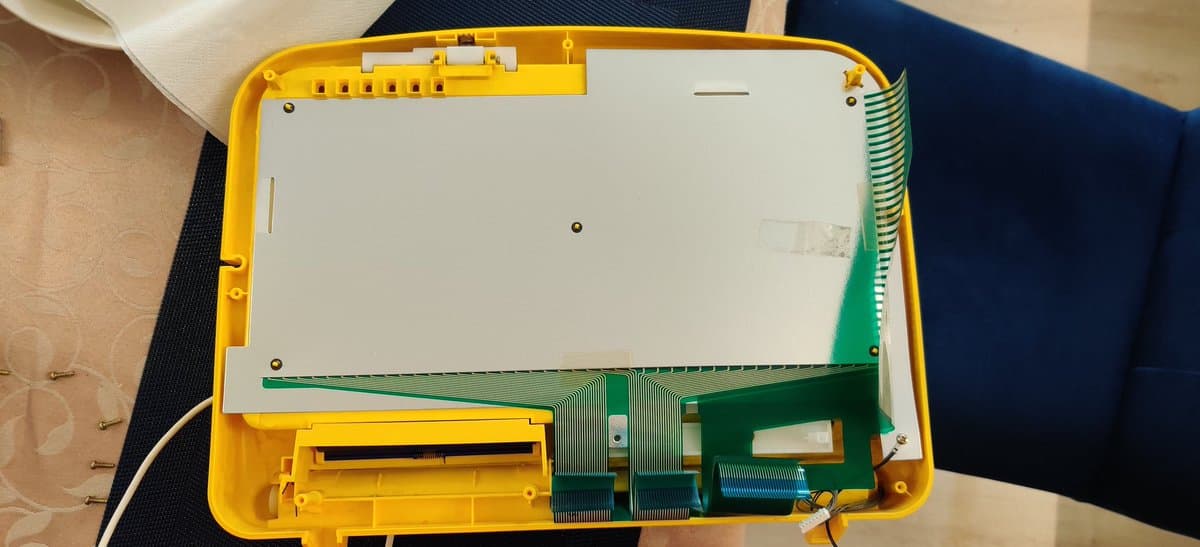 Interior of yellow Sega Pico with exposed motherboard showing green PCB, capacitors, and ribbon cable connectors after recap repair.