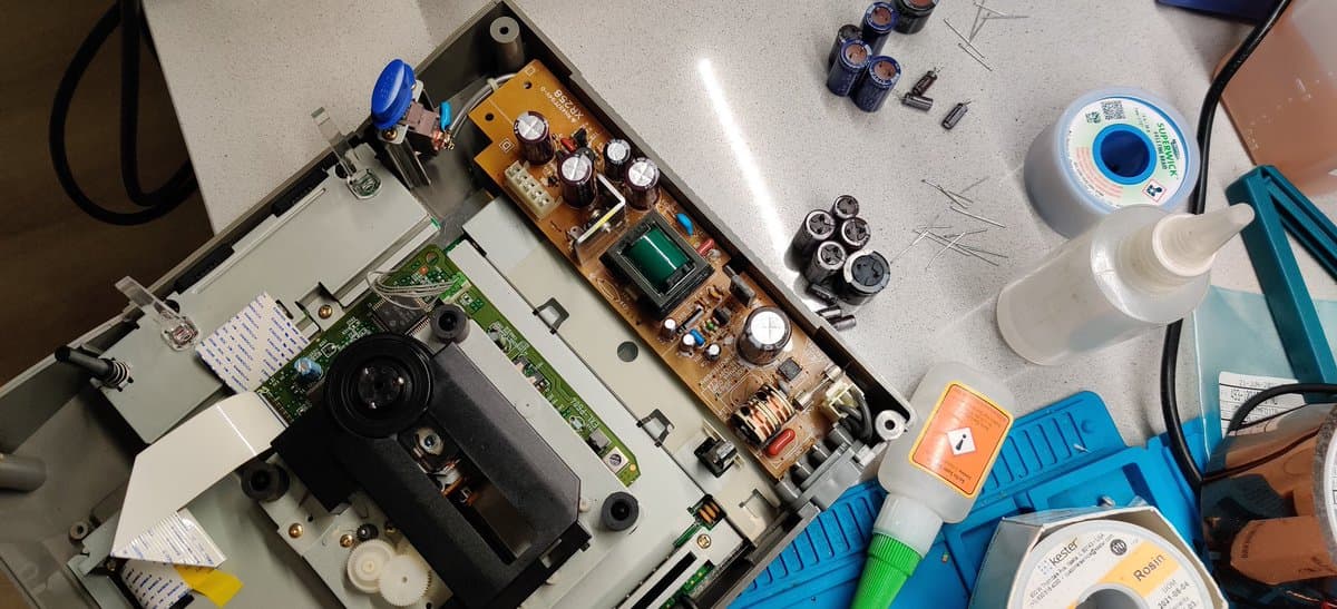 Disassembled Saturn PSU showing recapped circuit boards with replaced electrolytic capacitors, alongside soldering supplies and testing materials on workbench.