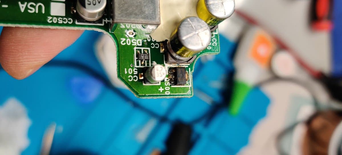 Leaked capacitors on NEC PC Engine GT controller input PCB being refurbished, with blue gloved hand holding board showing corrosion damage.