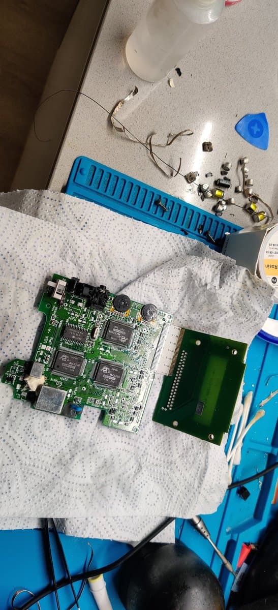 Disassembled PC Engine GT boards on paper towel with removed capacitors, blue organizer tray, desoldering tools, and flux-cleaned pads showing successful capacitor extraction without pad damage.