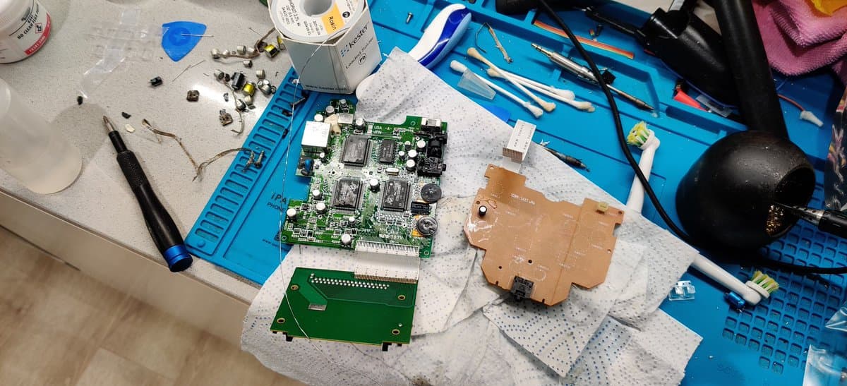 NEC PC Engine GT circuit boards during refurbishment: main board with new capacitors installed, controller board, and brown daughterboard on work mat with soldering tools nearby.