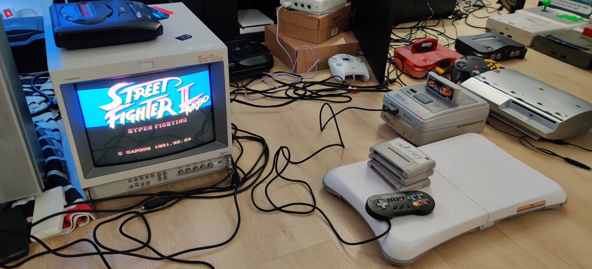Workbench with CRT displaying Street Fighter II Turbo, Satellaview unit, stacked SNES modules, controller, and various retro gaming hardware undergoing repair.