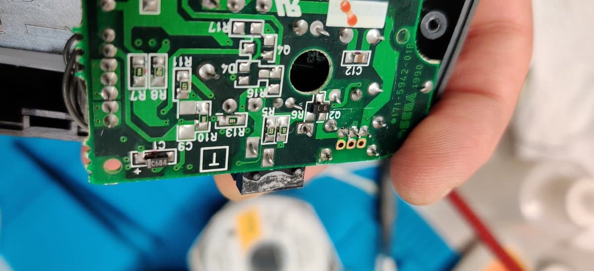 Sega Game Gear PCB held in hand showing reflowed solder joints and replaced capacitors during restoration work.