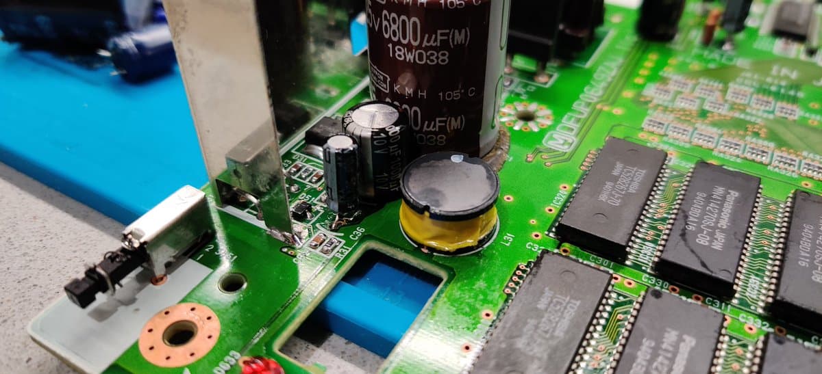 Panasonic FZ-1 PSU board mid-repair: large electrolytic caps, IC chips, bridged traces with solder, flux residue, and damaged through-holes from trace restoration work.