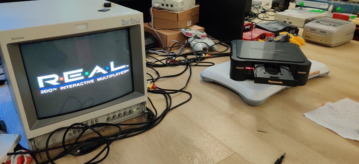 Panasonic FZ-1 3DO displaying boot screen on Hamilton monitor; repair workspace with soldering tools, capacitors, and Panasonic disc drive visible.